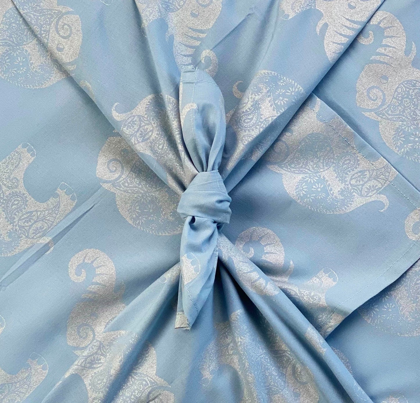 A fabric gift wrap with a sky-blue background featuring a silver paisley elephants design, tied in the center.