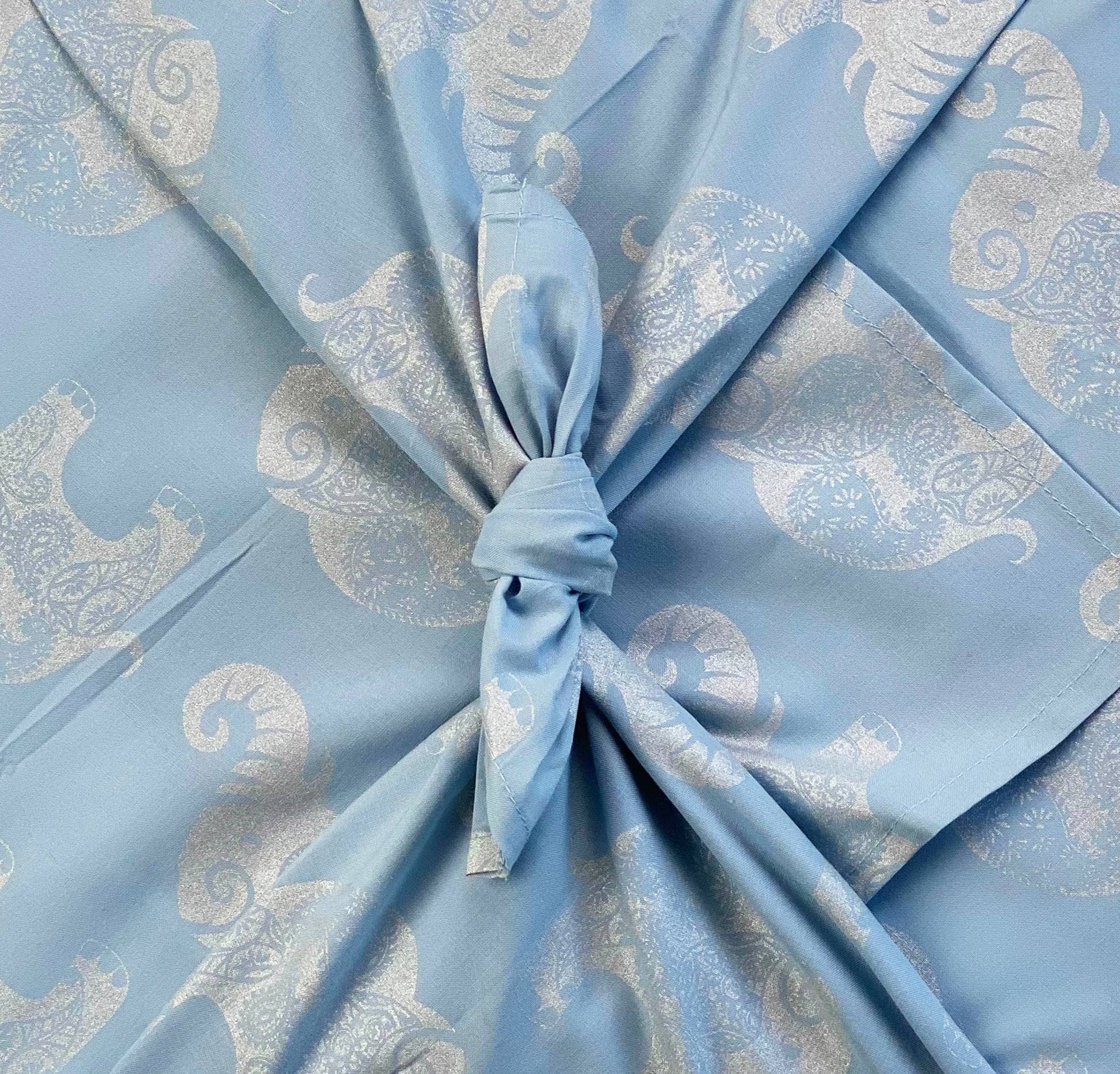 A fabric gift wrap with a sky-blue background featuring a silver paisley elephants design, tied in the center.
